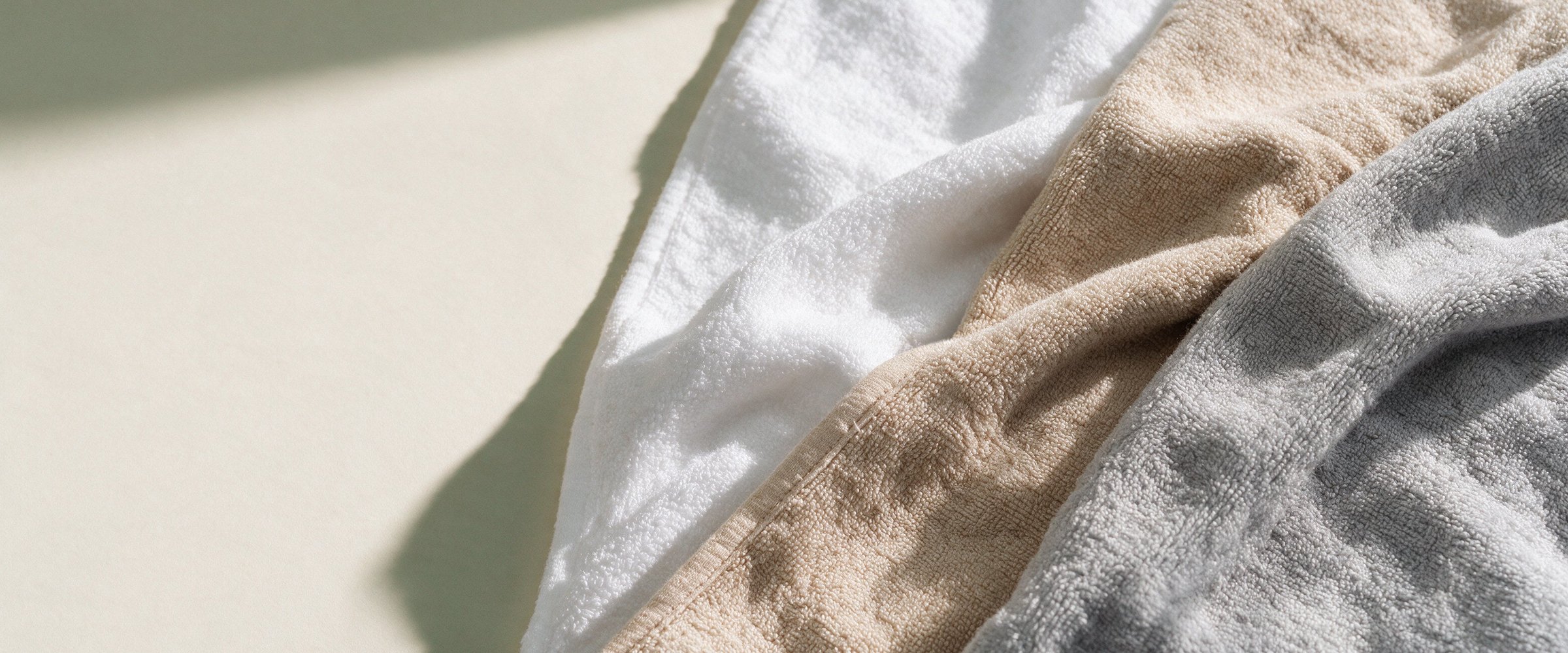 Close-up of soft white, sand and grey bamboo terry towels folded together in window light